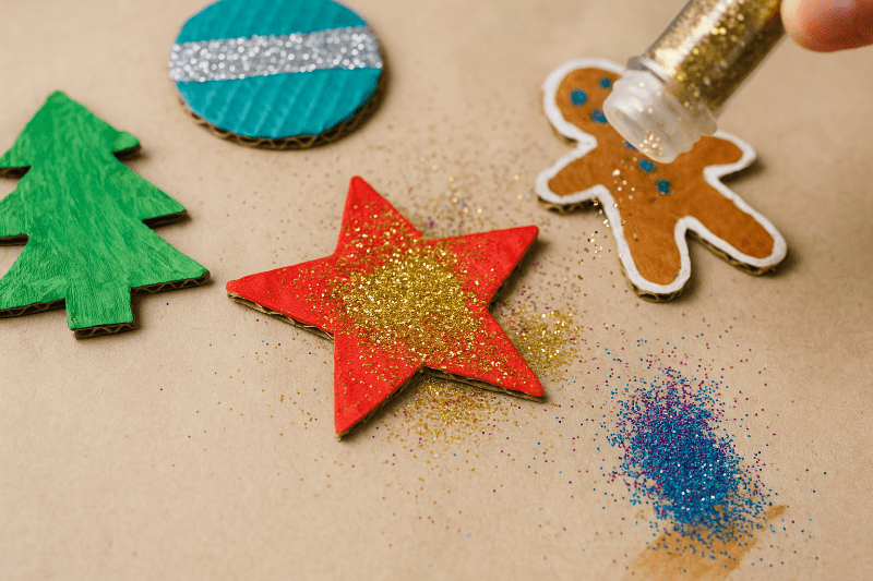 Dětské ruce sypou glitry na vánoční ozdoby z kartonu při tvoření.